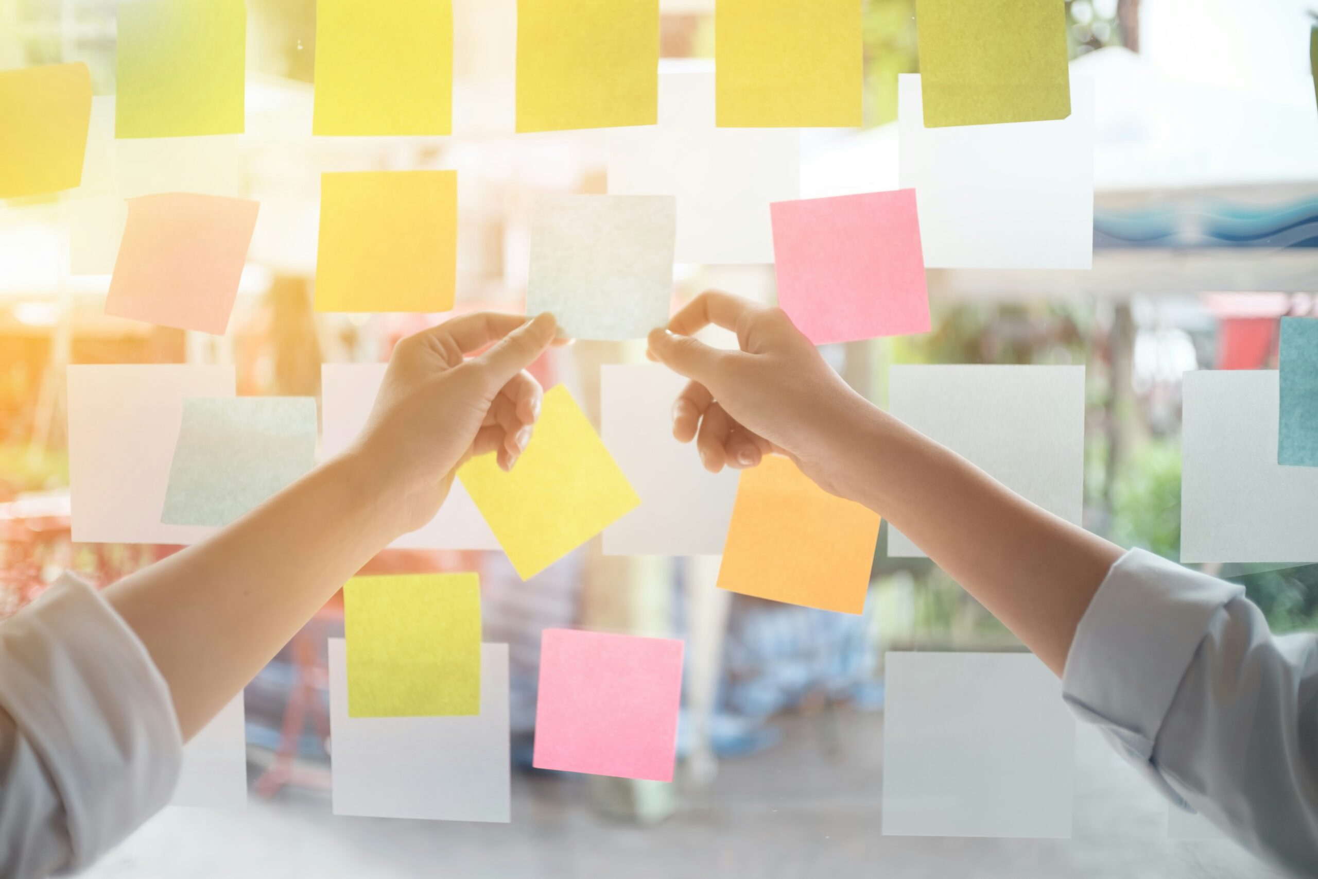 Mani che organizzano post-it colorati su una vetrata per definire analisi e strategia